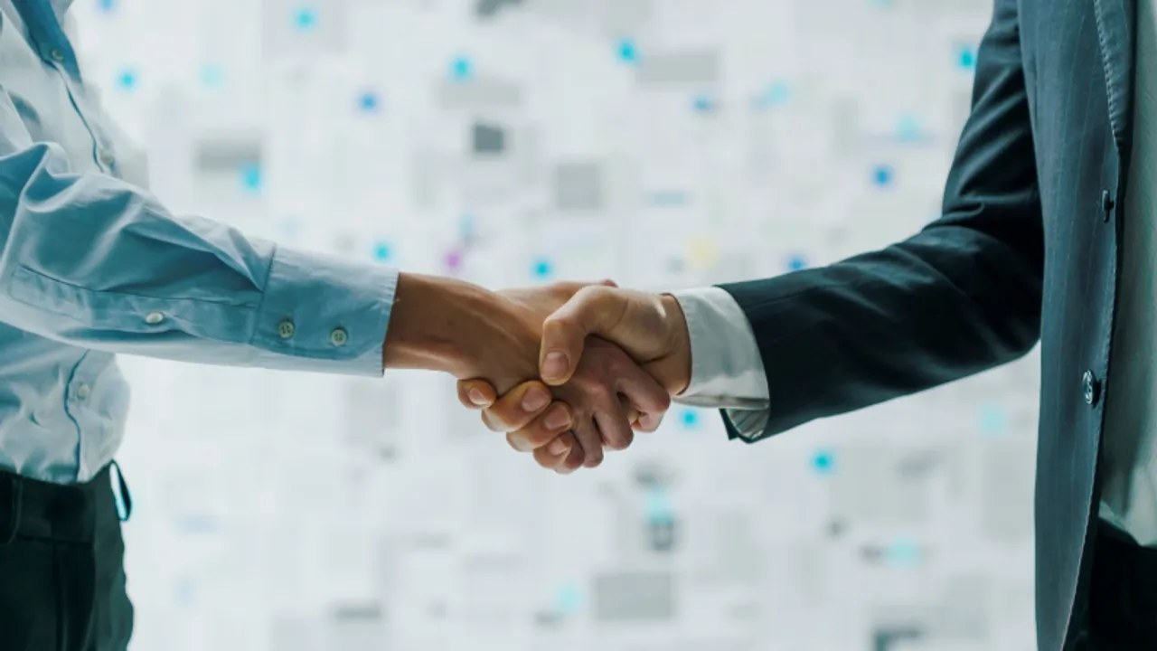 Close-up of a professional handshake between two people in business attire in a bright office.