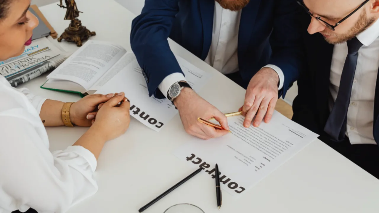 Attorneys and a client reviewing and signing a contract at a desk.