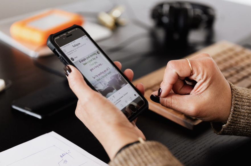 A person holding a phone showing a social media post while taking notes at a desk.